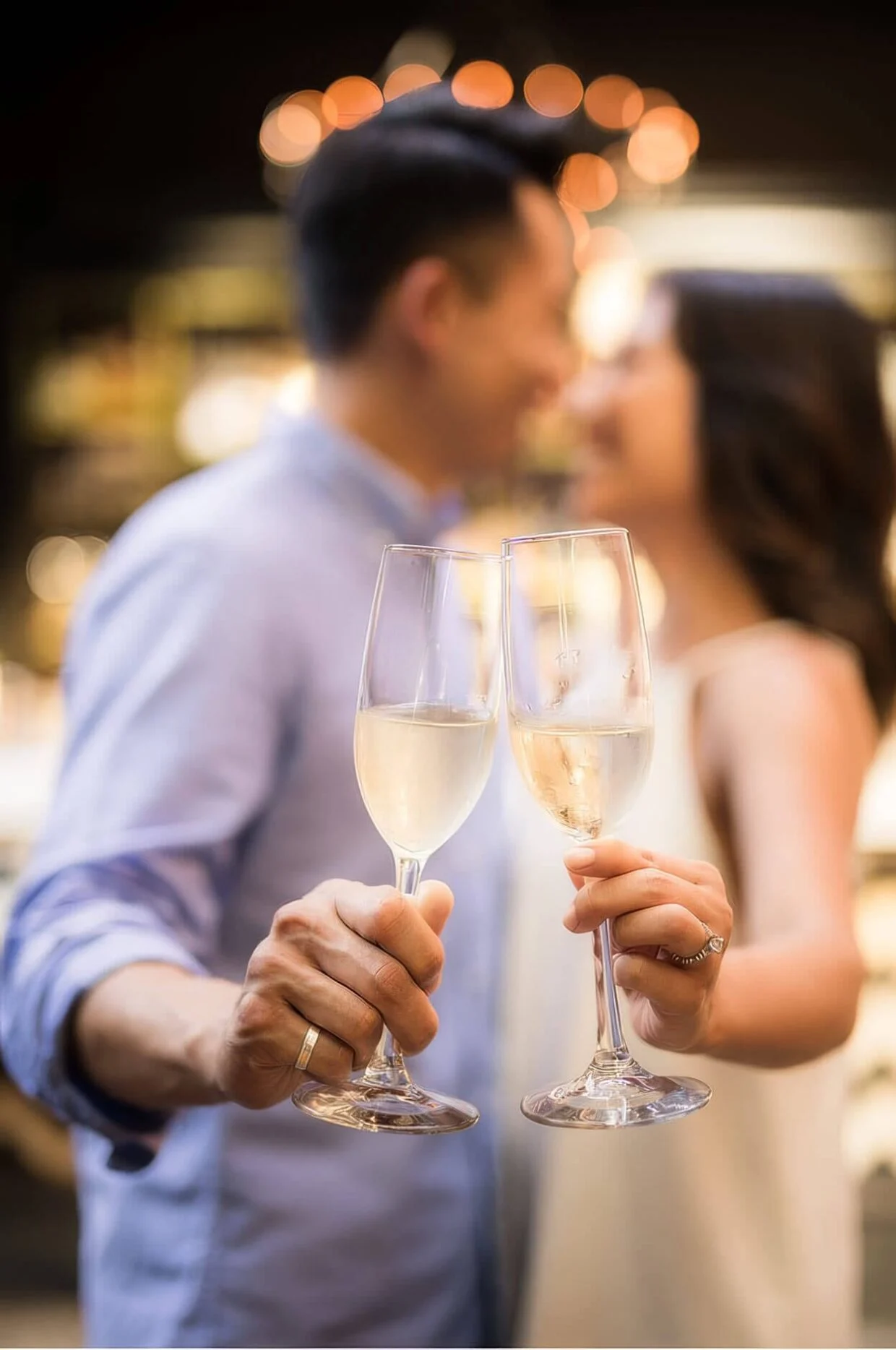 A couple touching two glasses of sparkling wine together under warm lights
